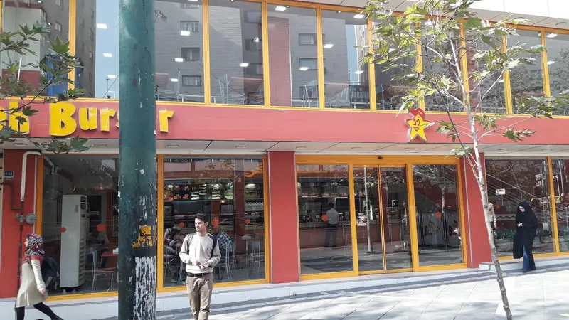 نمای کلی و روشن از شعبه استار برگر، رستوران فست فود محبوب با طراحی دو طبقه، نام تجاری برجسته و لوگوی ستاره لبخندزن.