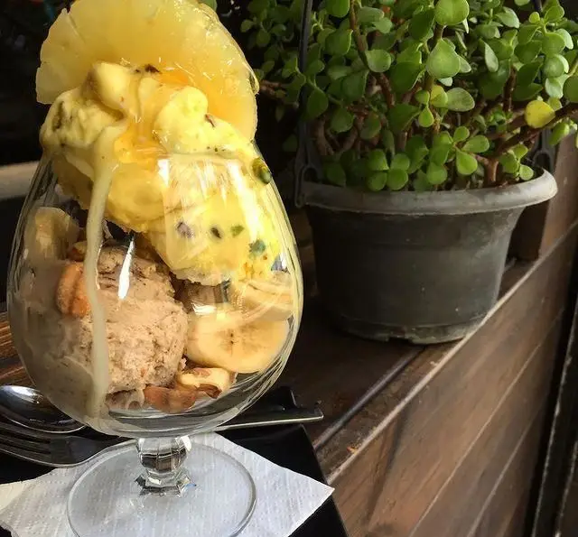 بستنی میوه‌ای هیجان‌انگیز با اسکوپ‌های آناناس، موز و مغز در لیوان شیک، دسری لذیذ و خنک از کافی شاپ تی شن.