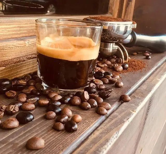 اسپرسو تازه و خوش عطر کافی شاپ تی شن با دانه های قهوه برشته شده و پودر قهوه در کنار پرتافیلتر، نمادی از کیفیت.