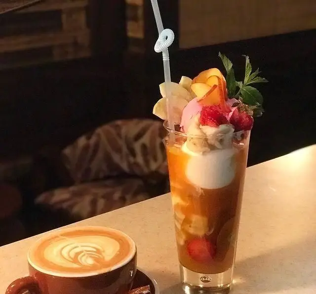 یک فنجان لاته با لاته آرت حرفه‌ای و دسری رنگارنگ شامل میوه، بستنی، توت فرنگی و نعناع در کافی شاپ تی شن.
