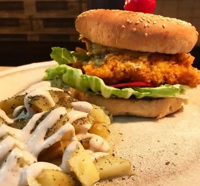 غذای خوشمزه کافی شاپ تی شن: برگر مرغ سوخاری لذیذ با نان کنجدی و سیب زمینی تنوری با سس سفید و سبزیجات.