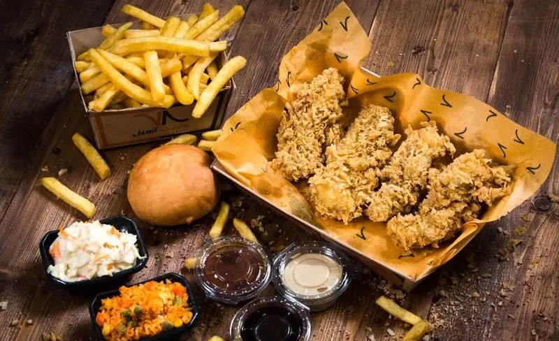 غذای خوشمزه سوخاری واویجه آهیل: فیله مرغ سوخاری کریسپی، سیب زمینی سرخ کرده، سالاد کلم، نان و سس‌های متنوع در بک گراند چوبی.