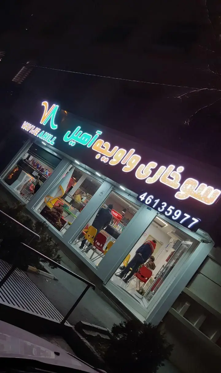 نمای شب رستوران سوخاری واویجه آهیل با تابلوی نئون درخشان، محیط داخلی و شماره تماس 46135977 جهت سفارش فست فود.