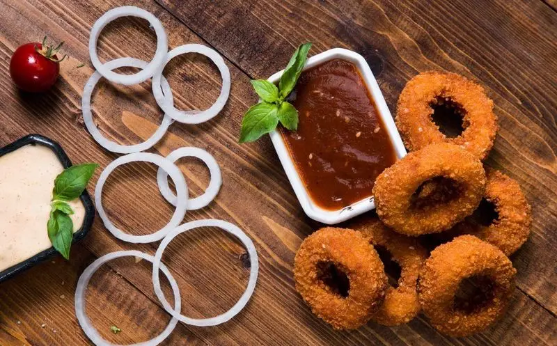 حلقه‌های پیاز سوخاری طلایی و خوشمزه واویجه آهیل با سس‌های مخصوص، آماده برای یک وعده غذایی لذیذ و دلنشین.