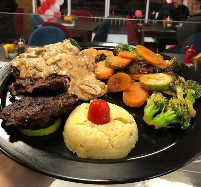 یک پرس کامل گوشت گریل شده با سس قارچ، پوره سیب زمینی و سبزیجات بخارپز تازه از فست فود گریل لند.