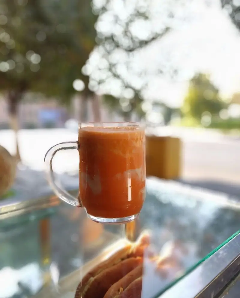 آبمیوه شهریور: لیوانی از آبمیوه تازه و خنک نارنجی رنگ، روی پیشخوان شیشه‌ای در یک روز آفتابی زیبا.