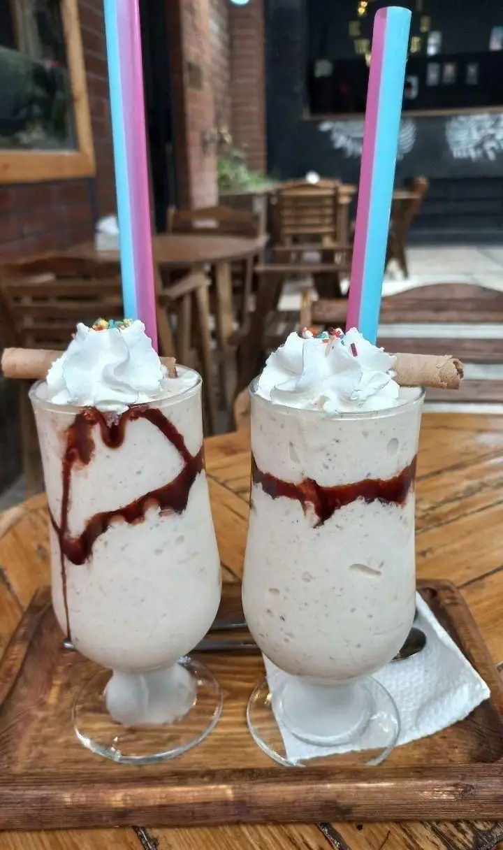 آبمیوه شهریور: دو میلک شیک خنک و دلچسب با تزیین سس شکلات، خامه، اسپرینکل و نی‌های زیبا. تجربه‌ای شیرین در کافه‌ی ما.