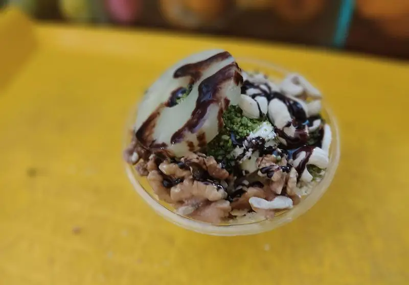 دسر میوه‌ای تازه و خوشمزه آبمیوه شهریور با تکه‌های گلابی، گردو، بادام هندی، پسته و سس شکلات روی میز زرد.