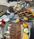 میز پر از دنده کباب، جوجه کباب و کباب کوبیده در فضای باز رستوران دنده کباب طاق بستان، همراه با مخلفات لذیذ و اصیل ایرانی.