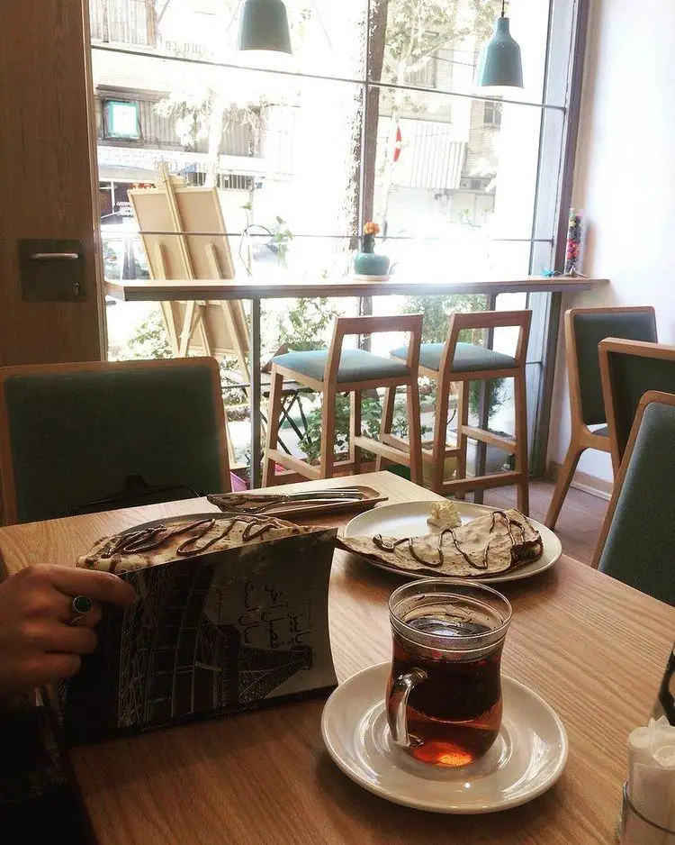 محیط داخلی دلپذیر کافه یاما با میزی چوبی حاوی چای گرم، دسرهای شکلاتی و منو. فضایی دنج و ایده‌آل برای یک تجربه کافه‌گردی آرامش‌بخش.