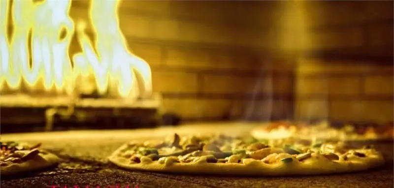 نمای نزدیک از پیتزاهای لذیذ در فر سنگی شعله‌ور رستوران تماشا، پخت بی‌نظیر برای تجربه‌ای فراموش‌نشدنی از غذا.