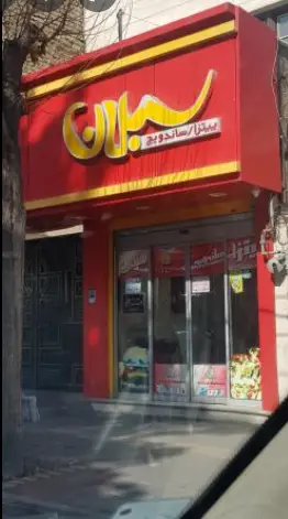 تصویر جذاب از نمای بیرونی پیتزا سبلان، رستوران فست فود با تابلوی قرمز و حروف برجسته طلایی "سبلان" و "پیتزا/ساندویچ".