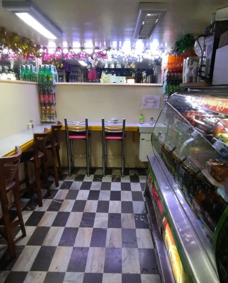 فضای داخلی ساندویچ نمونه، یک فست فود مدرن و تمیز با دکوراسیون شیک، کفپوش شطرنجی، کانتر، صندلی بار و یخچال نمایش نوشیدنی.