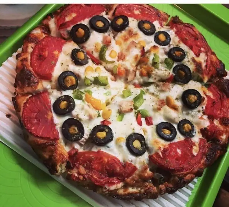 پیتزا مخلوط خوشمزه فست فود پاروت با تاپینگ‌های فراوان شامل سوسیس، کالباس، مرغ، زیتون سیاه و سبزیجات تازه، روی سینی سبز.