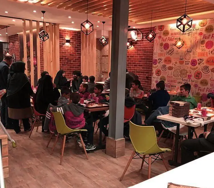 مشتریان شامل بزرگسالان و کودکان در فست فود پاروت، در محیطی با طراحی داخلی مدرن و جذاب با دیوارهای آجری و نورپردازی خاص.
