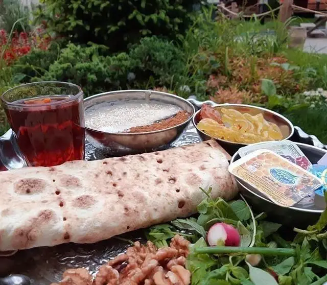 تجربه صبحانه اصیل ایرانی در کافه ایل بختیاری: نان سنگک داغ، چای، گردو، سبزی تازه، عسل و نبات در فضای دلنشین و سرسبز.