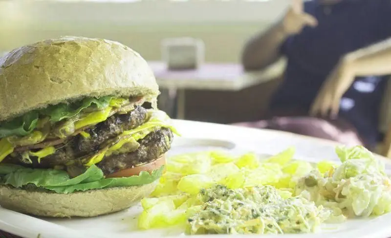 یک همبرگر دوطبقه بزرگ و لذیذ با نان سبزرنگ، کاهو، گوجه فرنگی، سس خردل و پنیر، به همراه سیب زمینی و سالاد تازه در رستوران وتوس.