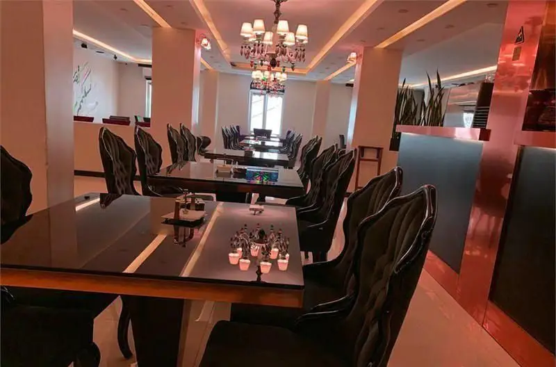 دکوراسیون داخلی لوکس کافی شاپ بوکالانج با میزهای براق، صندلیهای مخملی شیک، لوسترهای زیبا و نورپردازی گرم و دلنشین.