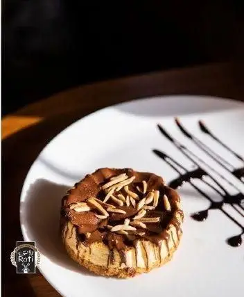 یک دسر وسوسه‌انگیز از کافه نان روتی: کیک شکلاتی کوچک با لایه‌ای از بادام روی سس شکلات، سرو شده روی بشقاب سفید.