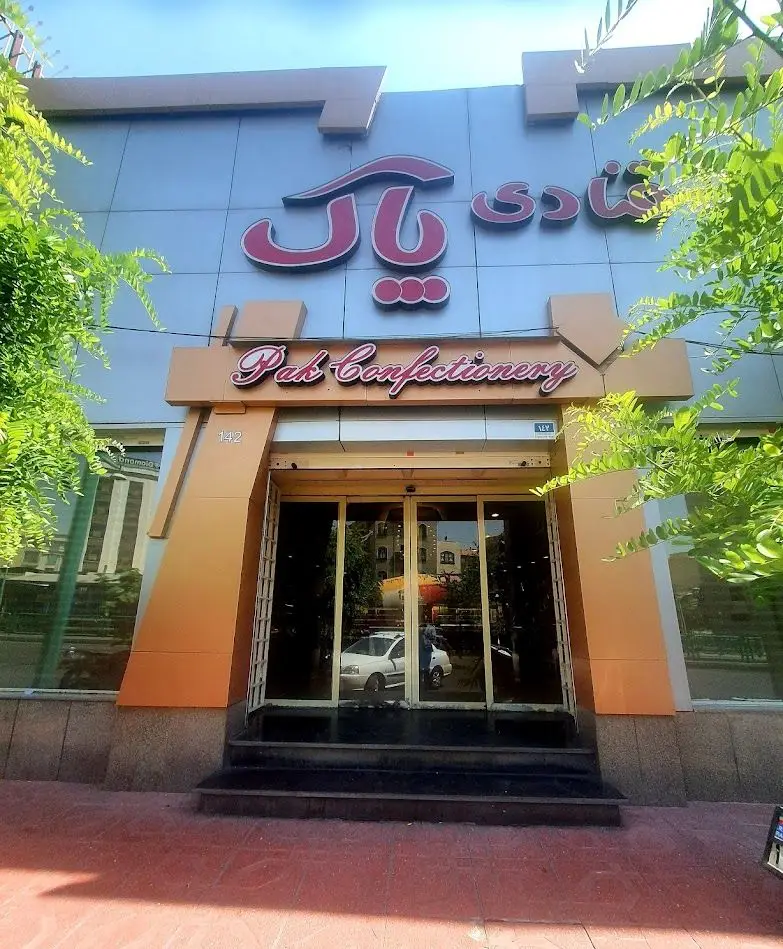 تصویر نمای بیرونی ساختمان فروشگاه شیرینی سرای پاک، یک قنادی مدرن با تابلو برجسته، نام فارسی و انگلیسی Pak Confectionery و ورودی اصلی.