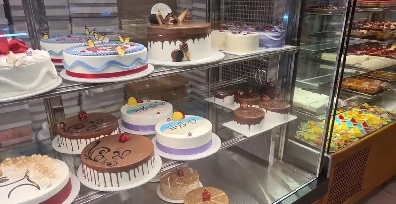 ویترین رنگارنگ شیرینی سرای پاک با انواع کیک‌های تولد، کیک شکلاتی، دسرها و شیرینی‌های تازه و خوشمزه برای جشن‌ها و مراسم.
