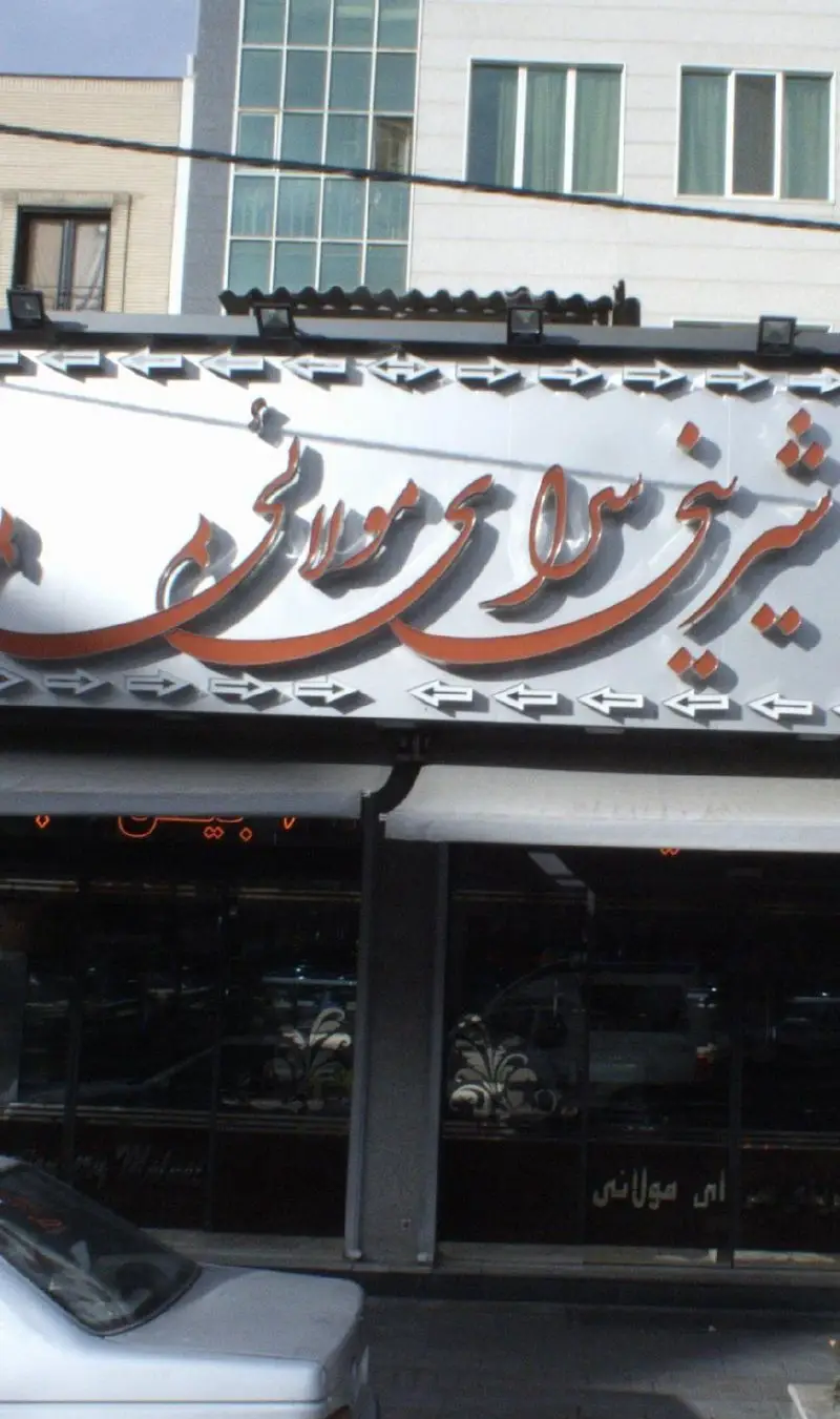 تابلوی مغازه شیرینی سرای مولائی با حروف برجسته نارنجی و فلش‌های سفید، نمای یک قنادی پرطرفدار با محصولات تازه و باکیفیت