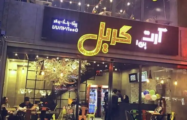 تصویری از نمای بیرونی رستوران ایتالیایی آرت گریل در شب، با تابلوهای نورانی بزرگ و اشاره به منوی پیتزا، پاستا و برگر.