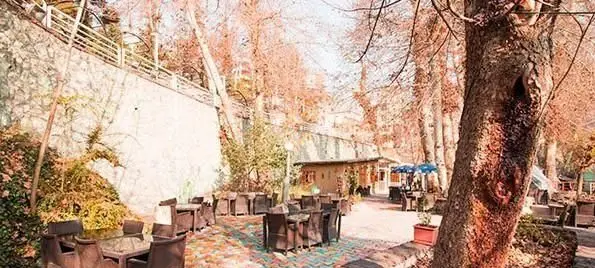 نمایی زیبا از فضای باز رستوران و کافه باغ مشیر در فصل پاییز، با میز و صندلی‌های چوبی و درختان نارنجی‌رنگ، مکانی دلنشین