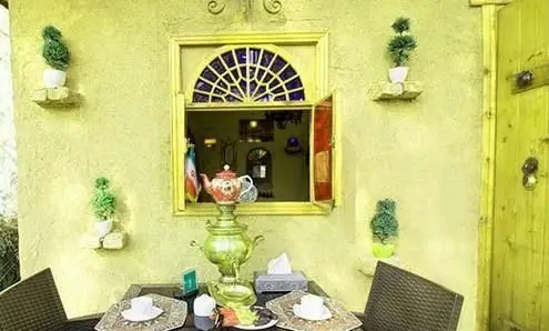 نمایی زیبا از فضای بیرونی رستوران و کافه باغ مشیر با دیوار زرد، پنجره سنتی، سماور و میز چای، محیطی دنج برای مشتریان.