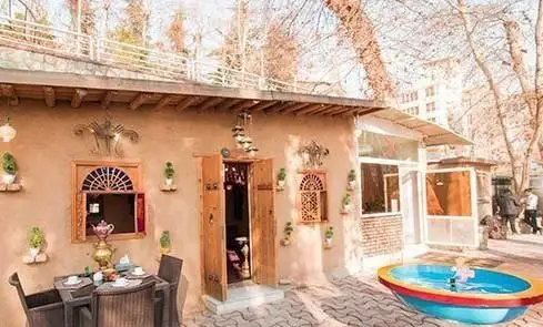 عکس از محیط بیرونی و دنج رستوران و کافه باغ مشیر، شامل بنای سنتی، حوض کوچک و آبنما، میز و صندلی برای صرف چای در فضای باز.