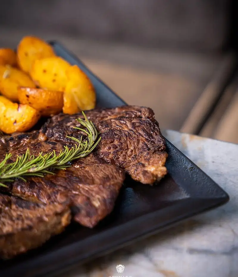 استیک گریل‌شده لذیذ با چاشنی رزماری و سیب‌زمینی‌های برشته طلایی، یک غذای اصلی محبوب از منوی ویژه رستوران ایتالیایی جنارو.