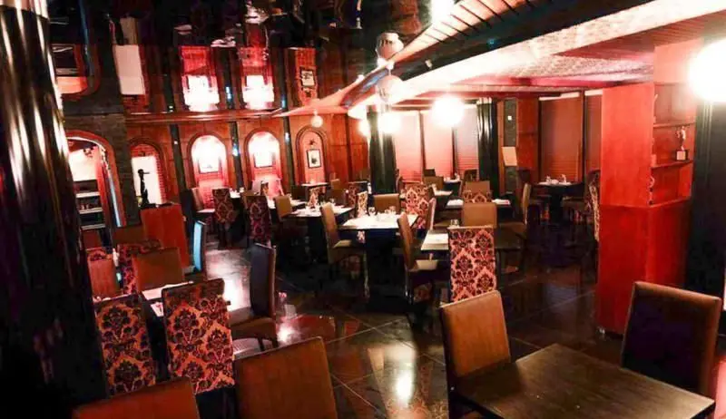 فضای داخلی دنج و دلنشین رستوران ایتالیایی جنارو با دکوراسیون چوبی و قرمز، میز و صندلی‌های راحت و نورپردازی گرم.