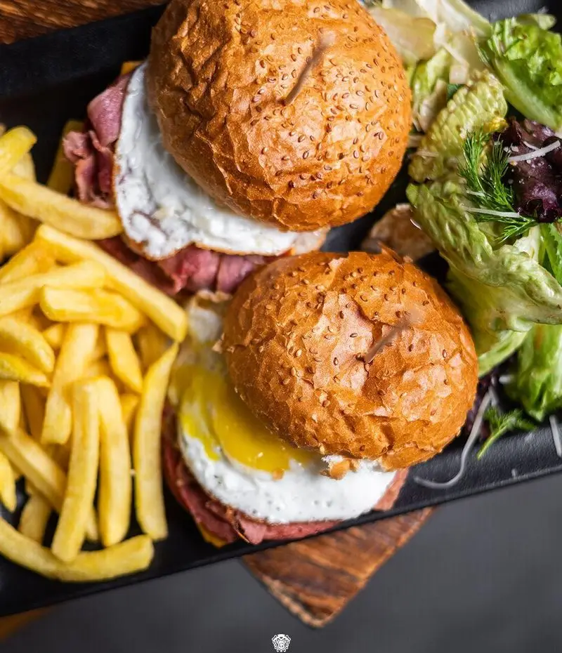 دو همبرگر یا ساندویچ مخصوص رستوران ایتالیایی جنارو با تخم مرغ، گوشت لذیذ، نان کنجدی، سیب زمینی سرخ کرده طلایی و سالاد سبز تازه.