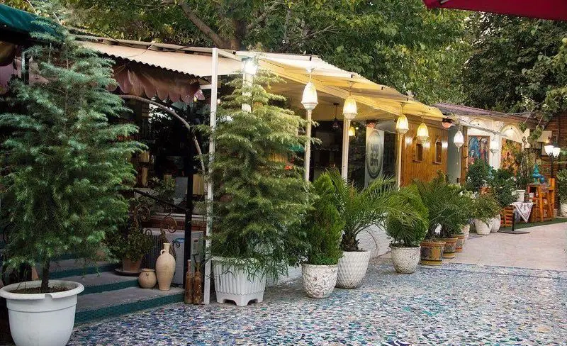 تصویری زیبا از فضای سبز و دلنشین کافه و رستوران باغ ایرو، با چیدمان گلدان‌های متنوع، نورپردازی گرم و حیاطی آرامش‌بخش در فضای باز.