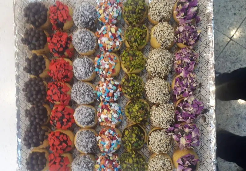 سینی پر از شیرینی‌های مدرن و خوشمزه قنادی مدرن شهر ری با تزئینات متنوع شامل شکلات، نارگیل، رنگی، پسته، کنجد و گل سرخ.