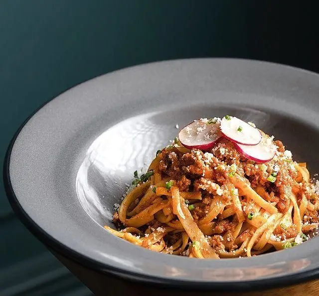 پاستا لذیذ با سس گوشت و پنیر پارمزان، تزئین شده با تربچه و پیازچه در کافه قنادی بیترسوییت. غذایی عالی برای ناهار یا شام.