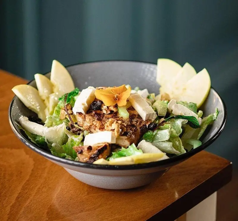 سالاد جذاب و رژیمی کافه قنادی بیترسوییت شامل مرغ گریل، کاهو، پنیر، سیب، گردو و گل خوراکی برای یک وعده سالم و لذیذ.