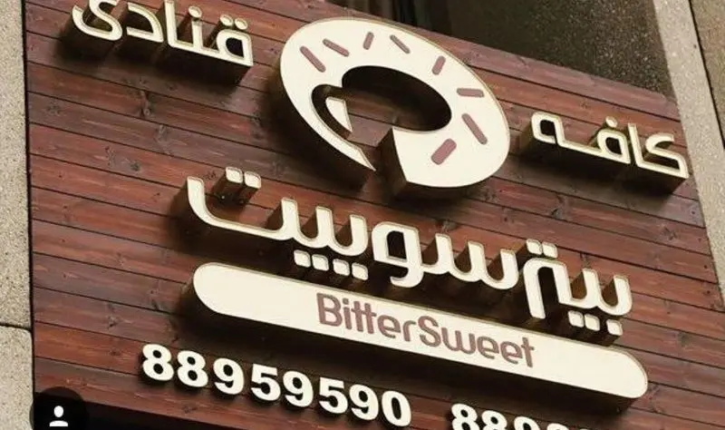 تابلو کافه قنادی بیترسوییت با لوگو دونات، نام BitterSweet به فارسی و انگلیسی و شماره تلفن ۸۸۹۵۹۵۹۰ روی زمینه چوبی قهوه‌ای.
