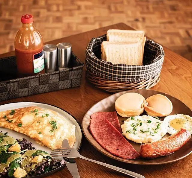 میز صبحانه مفصل کافه قنادی بیترسوییت با املت، سالاد، سوسیس، تخم مرغ، نان تست و مخلفات لذیذ بر روی میز چوبی.
