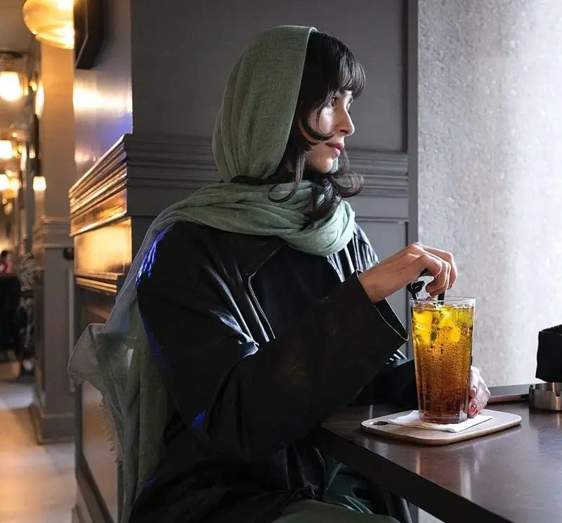 بانویی با حجاب سبز در کافه قنادی بیترسوییت نشسته و در حال لذت بردن از یک نوشیدنی خنک در فضای آرام و دلنشین.