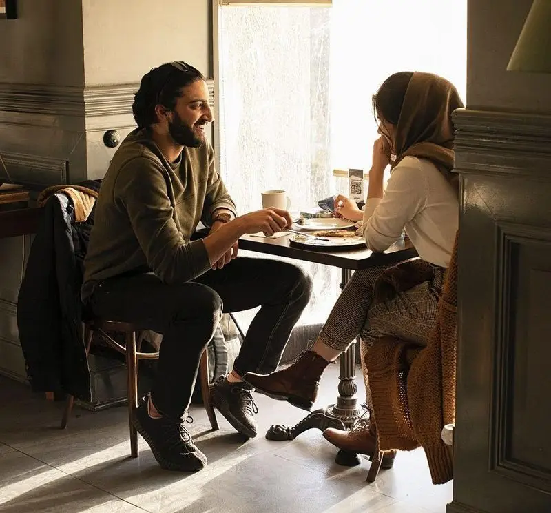 یک زوج با لبخند و گفتگو در حال صرف صبحانه در محیط گرم و آفتابی کافه قنادی بیترسوییت، لحظاتی دلنشین و به یادماندنی.