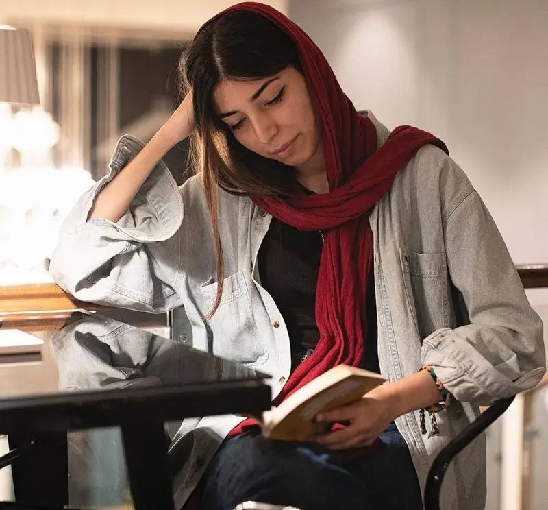 در کافه قنادی بیترسوییت، زنی جوان با روسری قرمز و پیراهن جین آبی، در فضایی آرام و دنج مشغول مطالعه کتاب است.