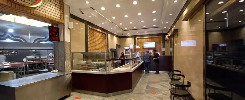 نمایی از فضای داخلی رستوران هانی مرکزی با آشپزخانه فعال، میز سرو غذاهای آماده و حضور مشتریان. محیطی تمیز و مدرن برای تجربه‌ی یک غذای لذیذ.