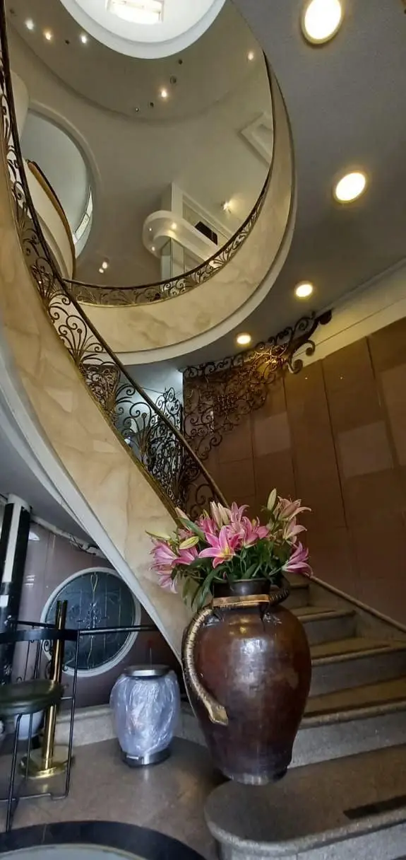 ورودی مجلل و دکوراسیون داخلی چشم‌نواز رستوران هانی مرکزی شامل راه پله مارپیچ با نرده‌های فرفورژه و گل‌های لیلیوم.