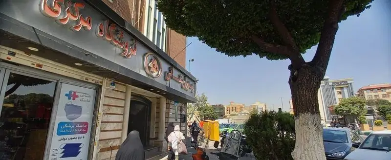 تصویر بیرونی رستوران هانی مرکزی، با تابلوی فروشگاه و پلاکارد ماسک، در یک خیابان شلوغ شهری با درختان و خودروها.