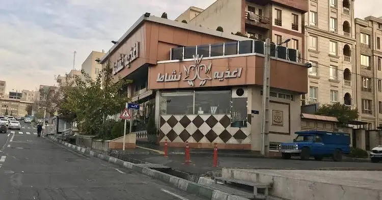 تصویر نمای بیرونی اغذیه نشاط در یک روز ابری. این کسب و کار محبوب فست فود و غذای آماده در خیابان اصلی تهران واقع شده است.