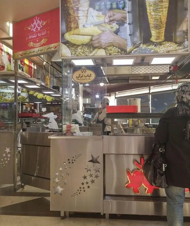 تصویری از داخلی اغذیه نشاط با تمرکز بر ایستگاه کباب ترکی و دونر. نمای آشپزخانه و آماده‌سازی غذای تازه در فست فود.