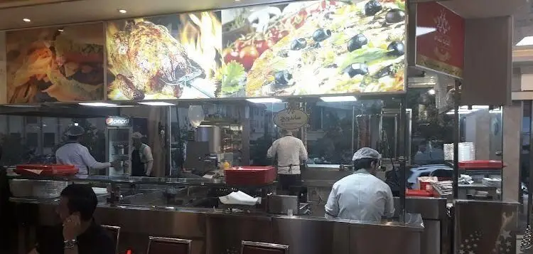 فضای داخلی و آشپزخانه فعال اغذیه نشاط با نمایش منوی پیتزا و مرغ بریان. پرسنل مشغول آماده سازی سفارشات ساندویچ.