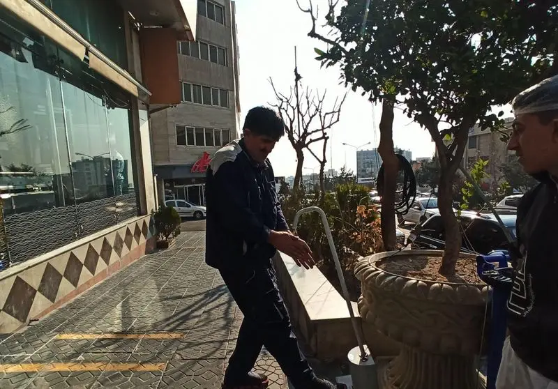 تصویری از نمای بیرونی اغذیه نشاط در یک روز آفتابی، با دو نفر از پرسنل در حال فعالیت روی پیاده‌رو جلوی رستوران.