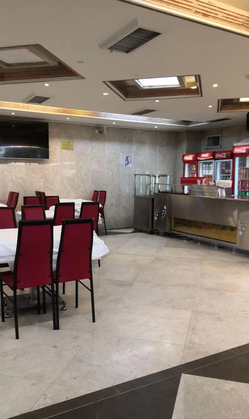 فضای داخلی شیک اغذیه نشاط، رستورانی با میز و صندلی های قرمز چیده شده، پیشخوان آماده سرو غذا و یخچال های نوشیدنی خنک.